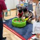 Two students are catching colorful fish at a green circular fishing pond set up at Shuqun Primary School, Singapore.