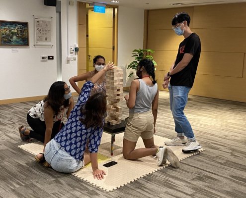 Adults enjoying a friendly game of Giant Jenga in Singapore, creating suspense and excitement with each turn.