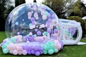 Large inflatable bubble dome used as an attraction at an outdoor carnival or festival, decorated with balloons