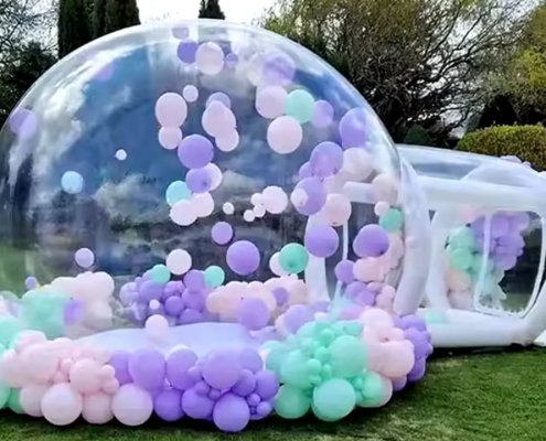 Large inflatable bubble dome used as an attraction at an outdoor carnival or festival, decorated with balloons