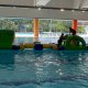 Inflatable water obstacle named 'Bells' with two circular platforms connected by a yellow balance pole, floating on water.