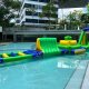 Cliff obstacle featuring a green and yellow triangular design with blue handles, part of a water sports inflatable challenge.