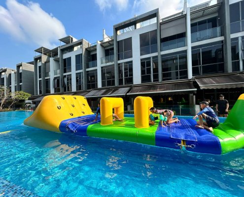 Participants crawl under square yellow inflatable arches on a water obstacle course at Belgravia Villas, Singapore