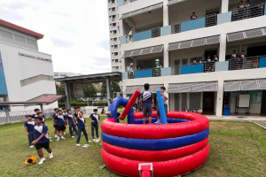 Students having fun on the Gladiator Dome at Canberra Sec School event in Singapore, standing on soft pedestals and using padded sticks.