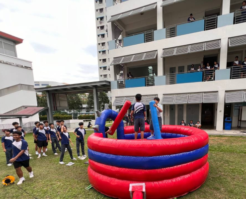 Students having fun on the Gladiator Dome at Canberra Sec School event in Singapore, standing on soft pedestals and using padded sticks.