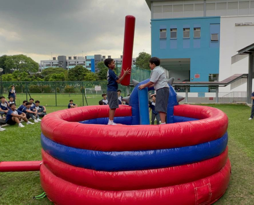 Two people playing on the Gladiator Dome inflatable game at Canberra Sec School event in Singapore, trying to knock each other off the platforms