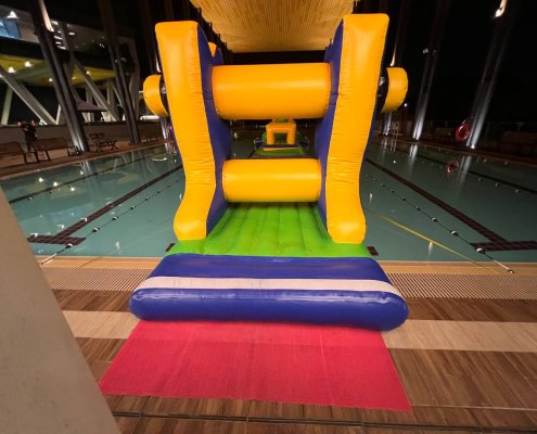 Close-up of the Grind inflatable obstacle, showing the wide gap between two large yellow padded rollers, designed for players to pass through easily.