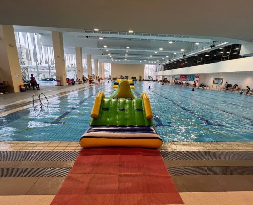 The Hill inflatable obstacle with a green slope, blue climbing handles, and yellow poles on each side for support.
