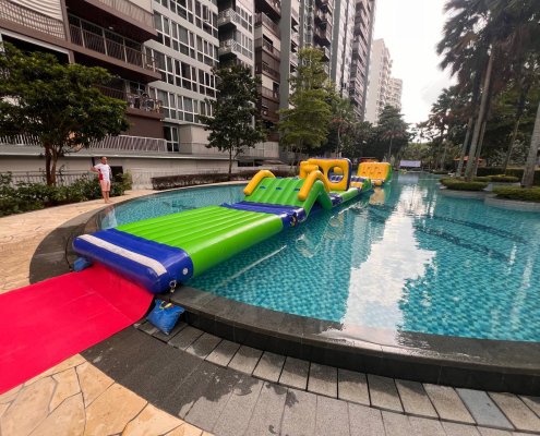 The Hill inflatable obstacle with a green climbing slope and blue handles, part of a floating water course.