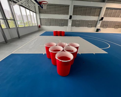 Human-size beer pong setup with large red buckets arranged in a triangle at Admiralty Lane, Singapore.
