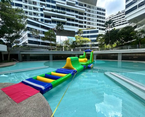 The Hurdle inflatable obstacle featuring three blue and yellow poles that participants must step across to avoid falling into the water.