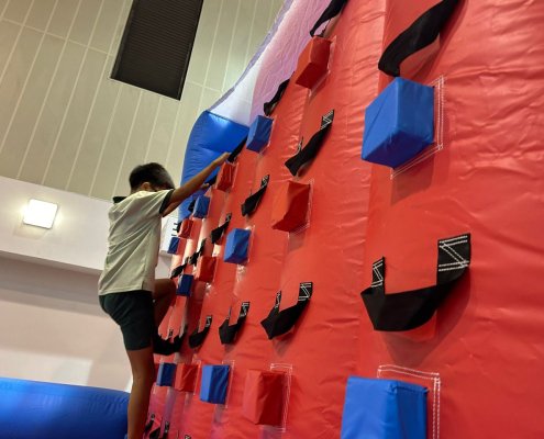 Children climbing a red inflatable rock wall inside the indoor sports hall of Farrer Park Primary School, Singapore.