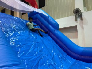 Children sliding down the blue inflatable slide attached to the rock wall inside the indoor sports hall of Farrer Park Primary School, Singapore.