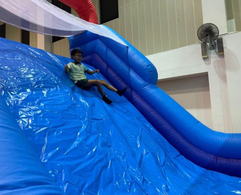 Children sliding down the blue inflatable slide attached to the rock wall inside the indoor sports hall of Farrer Park Primary School, Singapore.