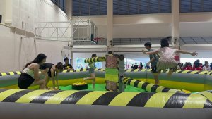 Children playing on the Meltdown inflatable game at National Junior College, Singapore, jumping to avoid the spinning padded arm.