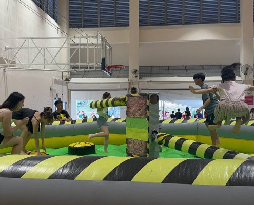 Children playing on the Meltdown inflatable game at National Junior College, Singapore, jumping to avoid the spinning padded arm.