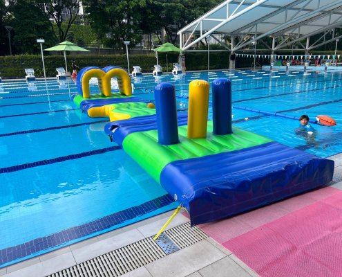 Pillars inflatable obstacle with two blue and one yellow upright columns on a green base, floating in a pool.