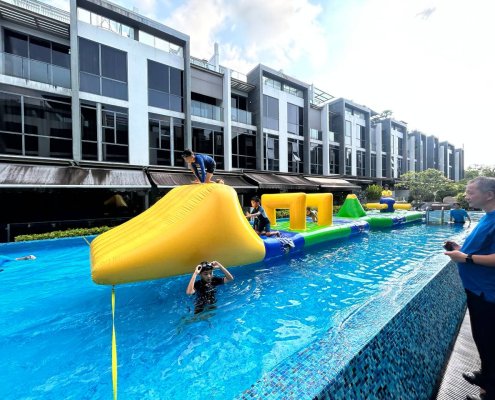A participant climbing up the yellow Slope inflatable using the blue handles, preparing to slide down into the water.