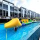 A participant climbing up the yellow Slope inflatable using the blue handles, preparing to slide down into the water.