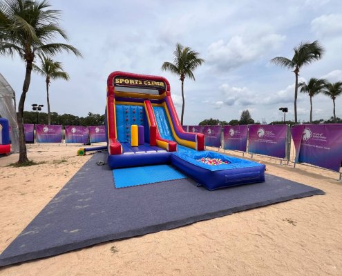 Inflatable Sports Climb game at Siloso Beach Walk, Singapore, showing a vibrant structure with wall climbing, a side slide, and three upright inflatable pillars before the wall.