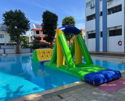 A large inflatable water obstacle with a triangular support pole and a rope hanging in the center for players to swing across.