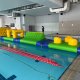 Inflatable water obstacle featuring a curved green structure with a yellow horizontal bar, challenging participants to balance through.