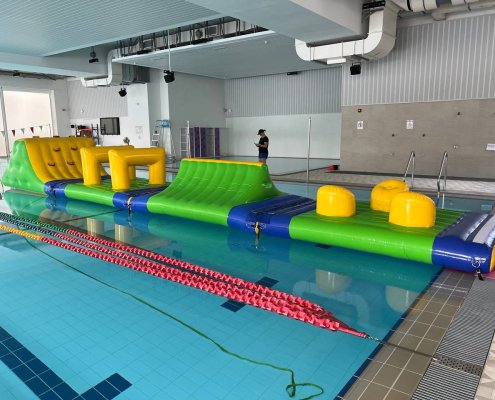 An inflatable obstacle with three rounded yellow humps on a flat green surface, designed for participants to jump or step across as part of a water course.