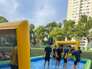 Water Soccer -Bishan Street Students at Bishan Street, Singapore laughing and kicking a ball on a bright blue and yellow inflatable water soccer field, splashing water as they play.