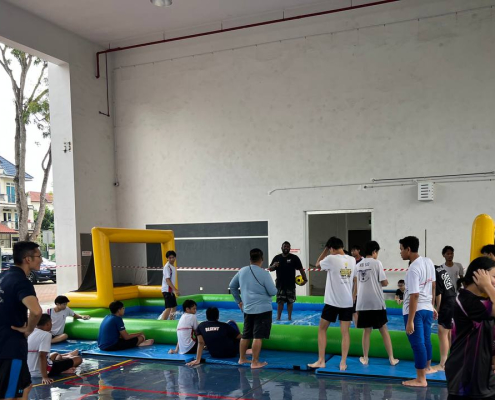 Water Soccer- Regent Secondary School 1 Excited students at Regent Secondary School chasing the ball in a fun-filled water soccer game, surrounded by splashes and bright inflatable walls in blue and yellow, Singapore.