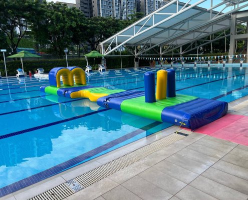 A flat green inflatable platform with wavy, curved edges, part of a water obstacle course.