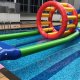 Two long, parallel green inflatable poles floating on water, forming a lane for players in a water obstacle course.