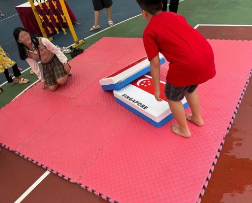 Two players competing in the Giant Country Eraser game on a padded mat at an event in Singapore.
