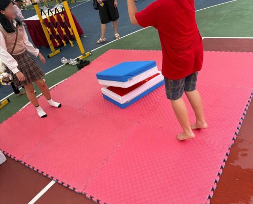 Players taking turns in the Giant Country Eraser game on a soft mat in Singapore, each trying to flip their eraser to the top.