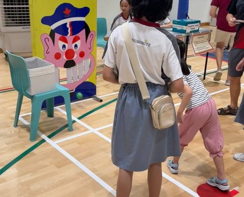 Children aiming soft balls at the cartoon face, trying to knock out as many teeth as possible — full of energy and fun at Shuqun Primary School, Singapore.