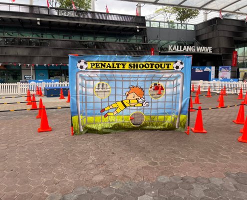 The Penalty Shootout game shows a printed goalkeeper on a banner with three cut-out holes as targets, inviting players to test their football skills at OCBC Square, Singapore
