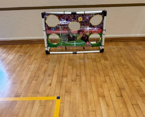A soccer-themed challenge with a goal covered by a banner with five circular cutouts, designed for players to test their aim and accuracy at Gongshang Primary School.