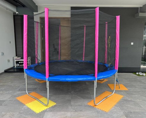 A clean, fully assembled trampoline with blue or pink padding standing in an indoor space, ready for rent at Jalan Khairuddin, Singapore.