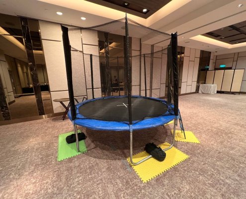 A trampoline in bright blue colors featuring strong safety poles and netting, ready for fun at The American Club, Singapore.